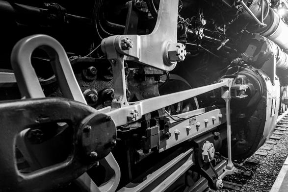 The image is a black and white photograph of the undercarriage of a steam locomotive. The focus is on the intricate mechanical components, including large metal beams, bolts, and wheels. The beams are painted white, contrasting with the darker metal parts. The wheels are visible, with one prominently in the foreground, showcasing the complex gear system and connecting rods. The background is blurred, emphasizing the detailed machinery in the foreground. The image captures the industrial design and engineering of the locomotive, highlighting the robustness and complexity of the components.

Provided by @altbot, generated privately and locally using Ovis2-8B