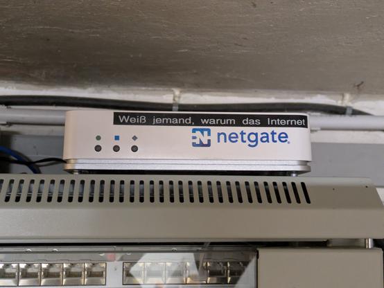 Firewall des Herstellers Netgate, über deren Logo ein Aufkleber mit der Aufschrift "Weiß jemand, warum das Internet..." angebracht ist