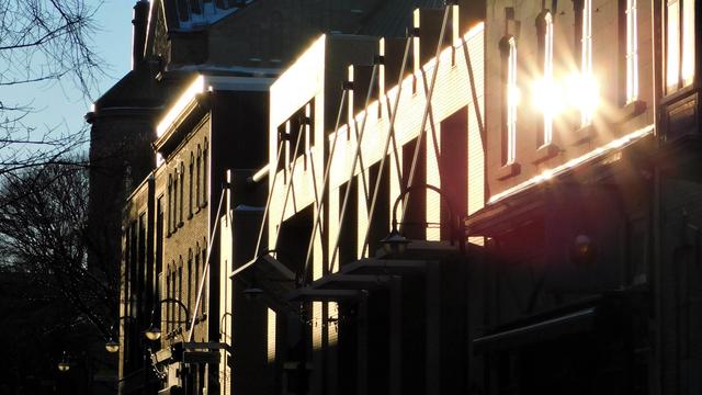 Dans une rue, le soleil se reflète sur les fenêtres d’un immeuble, illuminant toute la scène. 
© 2025, Chartrand Saint-Louis, photographie