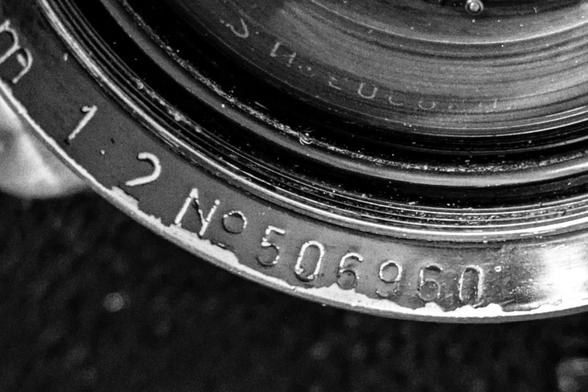 Close-up of the serial number on a camera lens. The paint is worn on the leading edge, but the raised lettering makes it still readable.