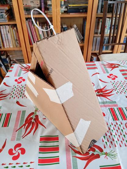 Structure en carton,  triangulaire, en 3D. Il y a une boucle en plastique au sommet de la structure, et je n'ai pas encore refermée l'une des faces triangulaires, afin de pouvoir mettre les bonbons. Du scotch de masquage maintient une des faces triangulaires contre les côtés de la structure, le temps que la colle sèche.