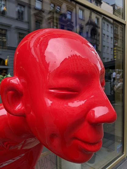 Huge red smiling polished resin head in a pedestrian zone