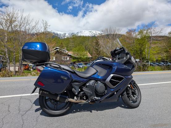 A blue sport touring motorcycle parked on the side of the road with a snow capped mountain in the background