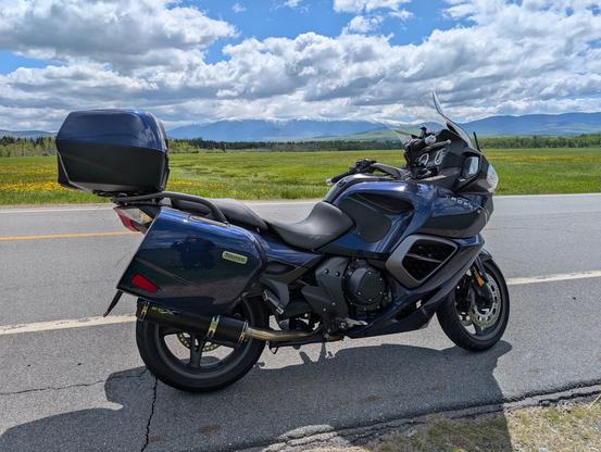 A blue sport touring motorcycle with a green field in the background, and mountains in the far distance