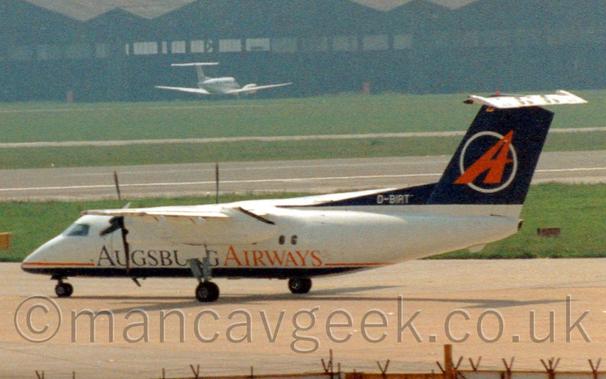Side view of a high-winged, twin propellor-engined airliner taxiing from right to left.
The plane has a white body, with a blue belly, and a red pinstripe overlaid with blue and red "Augsburg Airways" titles.
The tail is dark blue, with a red upper-case letter "A" leaning to the right, with the white outline of a circle behind it.
Grey concrete apron fills the foreground, with grass either side of a black runway in the background leading up to a wide black hangar that stretches across the frame, with a white BizProp parked in front.