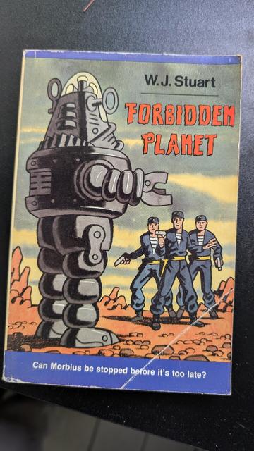 Photograph of a book cover of forbidden planet with sci-fi artsy drawing of robots and spacemen
