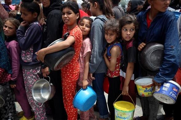 Des Palestiniens font la queue pour recevoir un repas chaud à un point de distribution de nourriture dans le quartier d'Al-Rimal à Gaza, le 22 mai 2025. © Photo Majdi Fathi / NurPhoto via AFP