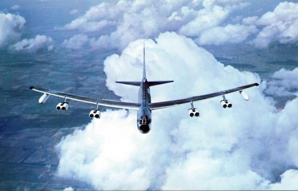 An almost head on shot of a plane in flight. you are slightly above looking down. There are puff clouds around