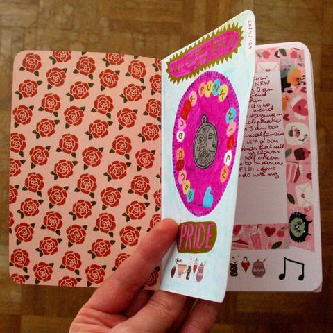 Artjournal that is held open on the first page with a title page that says "Witches' Black Lent" and "PRIDE" and a sketch for a bright pink amulet in the middle.