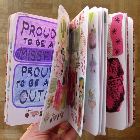 Artjournal that is held open so several pages are visible. On one pages the words "Proud to be a missfit. Proud to be an outcast." are partly visible and on other pages there are stickers and collages.