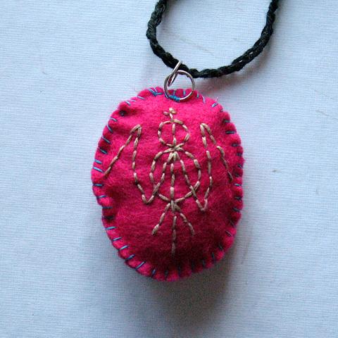 The other side of the bright pink felt amulet with an embroidered sigil.