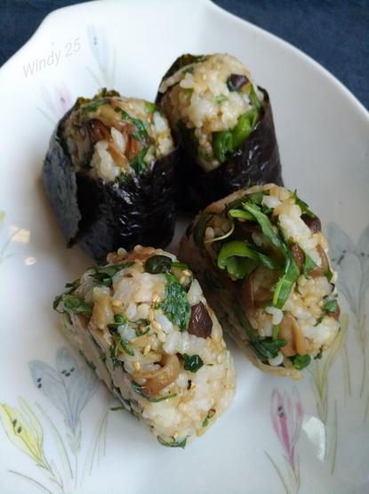 4 onigiri triangular shaped rice balls on a plate. 2 are wrapped in nori seaweedpaper, 2 are without so the mixed ingredients in the rice would be visible.