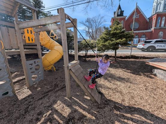 A child uses a rope to climb a playground structure.