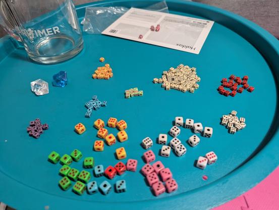 A collection of tiny six-sided dice are sorted on a round blue table.