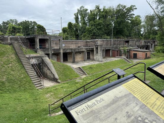 The image depicts Fort Hunt Park, showcasing a series of concrete structures with multiple levels and staircases. The buildings are constructed from gray concrete, with some areas featuring brick accents. The site is surrounded by green grass and trees, indicating a park-like setting. In the foreground, there are informational signs with the text "Fort Hunt Park" visible, providing historical context. The structures appear to be part of a historical fortification, with openings and doorways suggesting former military use. The sky is overcast, and the overall atmosphere is one of historical significance and tranquility.

Provided by @altbot, generated privately and locally using Ovis2-8B

🌱 Energy used: 0.152 Wh