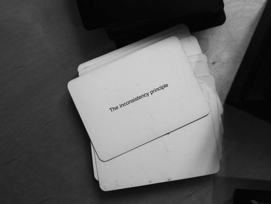 A black-and-white photo of an Oblique Strategy card. The card reads: 'The inconsistency principle'.