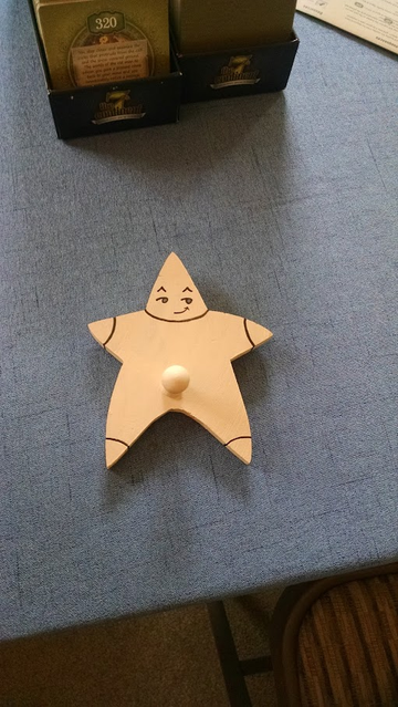 A wooden star-shaped hanger purchased years ago from Joann's. There is a single peg at the bottom between the two star 'legs'.

Lines have been painted on the hanger to make it look like a star-shaped person. There is a very saucy side-smirk on its face.