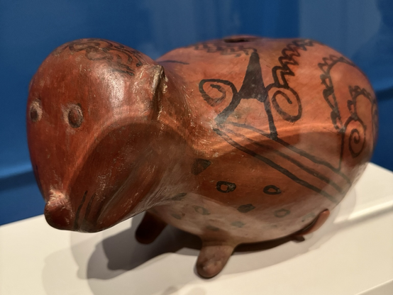photo of the Paca effigy vessel on display at museum, fuller side profile Redware ceramic with black geometric painted designs on body