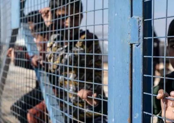 Des enfants derrière les grilles d’un camp.