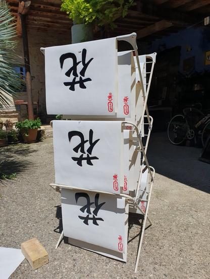Large white sheets marked in black ink with japanese kanji set out to dry in the sun on a clothes horse