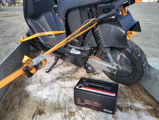 Escooter (Vespa like not kid-like) with missing body panels. Battery in front looking much like a 12V car battery but supposedly gives 2kWh & 75km of range