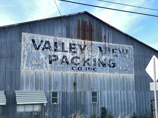 Photo of a weathered sign painted on the side of an aluminum building. It reads “Valley View Packing”.