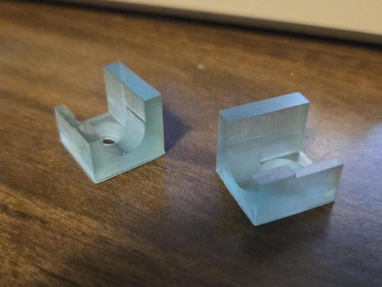 A pair of translucent blue pieces of plastic in an uneven U shape with a tapered hole in the bottom and a partial circle cut out of the side to hold a "hinge rod".