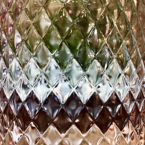 Close-up of water pitcher with a rhombus pattern surface, reflecting various colors and lights from objects behind it.