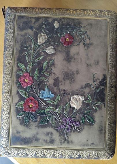A very old leather-bound book slightly less than a hand-wide tall.  The leather is embossed with a gold border and a bouquet of flowers in red, light blue and white.  The shape of the bouquet forms a letter C tilted backwards to the left and  is tied with a lavender bow.  The leather is worn and dry, a small tear at the top of the spine is visible.