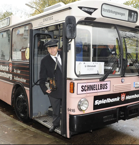 Ein alter rosa Schnellbus. Aus der geöffneten Vorder Tür schaut ein Busfahrer in Uniform mit umgehangten Geldwechsler.