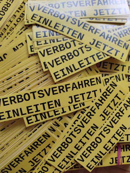 Viele Sticker, schwarze Schrift auf senfgelben Hintergrund mit dem Text: Verborsverfahren einleiten jetzt!