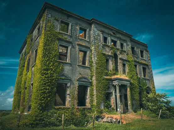 A sideways view of an abandoned large building with vines growing through the empty windows,