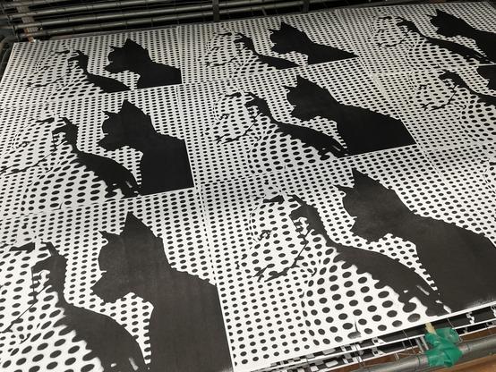 nine  prints lie next to each other in a drying rack. The pictures all show the same motif: a naked, torso with a dog mask on its  head in the projection of a grid. The person can be recognised by the deformation of the grid and their shadow.
