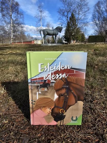 Kuvassa Esteiden edessä -kirja ja taustalla näkyy hevospatsas.
