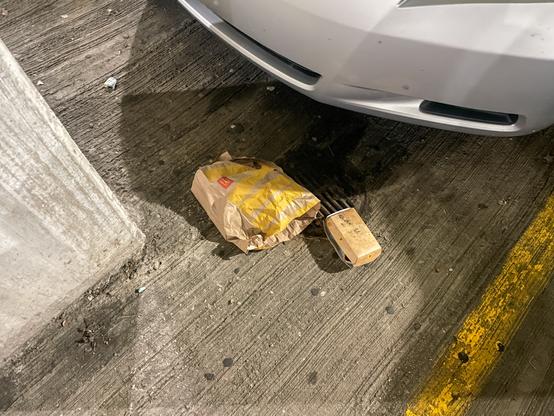 Paper bag and cardboard container from McDonald's on a cement parking spot next to a silver car.