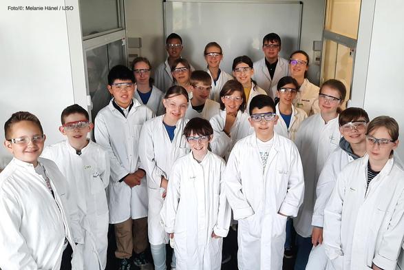 Die IJSO-Juniorforscherinnen und -forscher in Laborkitteln und mit Schutzbrillen bei den JuniorForscherTagen 2025 auf dem Gutenberg-Campus in Mainz (Foto/©: Melanie Hänel / IJSO)