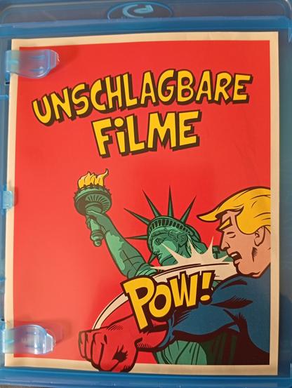 Prospekt in einer Blu-ray Hülle. Überschrift "Unschlagbare Filme". Comiczeichnung. Ein Mann, der auffällige Ähnlichkeit mit Donald Trump hat, verpasst der Freiheitsstatue einen Faustschlag. Davor der Text "POW!".