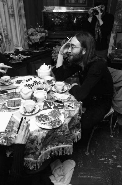 Fiktive Bildbeschreibung – John Lennon und die Geburtsstunde der Schwingungsidee

London, Winter 1970 – ein Morgen, der später in keine offizielle Biografie eingehen würde, aber in den Zwischenräumen der Geschichte schwingen geblieben ist.

John Lennon sitzt an einem schweren, blumengedeckten Teetisch in einem alten viktorianischen Haus – die Vorhänge fast zugezogen, ein Teekessel pfeift leise aus. Auf dem Tisch liegen Notizen mit der Aufschrift WAR IS OVER und ein halbfertiges Manuskript mit dem kryptischen Titel: „Klang als Heilung – erste Skizzen zur Ontologie der Schwingung“. Niemand ahnt, dass es weniger um Politik als um Frequenz geht.

„Stell dir vor, es gäbe keine Grenzen“, murmelt Lennon, während er sich eine Zigarette anzündet. Der Satz klingt beiläufig – aber im Raum verändert sich etwas. Nicht durch Worte, sondern durch Schwingung. Die Kamera im Hintergrund hält diesen Moment fest, doch das eigentliche Ereignis bleibt unsichtbar.

Die Frau, deren Hände man nur sieht, stellt ihm Fragen – keine Journalistin, sondern eine Physikerin aus Zürich, die an einem Vortrag zu „Resonanzfeldern in kollektiven Bewusstseinsräumen“ arbeitet. Lennon hört aufmerksam zu. Es geht nicht mehr nur um Musik. Es geht um Frequenzen, um Weltbilder, um die Idee, dass Disharmonie kein moralisches, sondern ein energetisches Problem sei.

„Was, wenn jedes Unrecht, jeder Krieg, nichts weiter ist als ein entgleistes Schwingungsmuster?“, fragt sie.

„Dann ist Imagine nicht nur ein Lied“, sagt John
