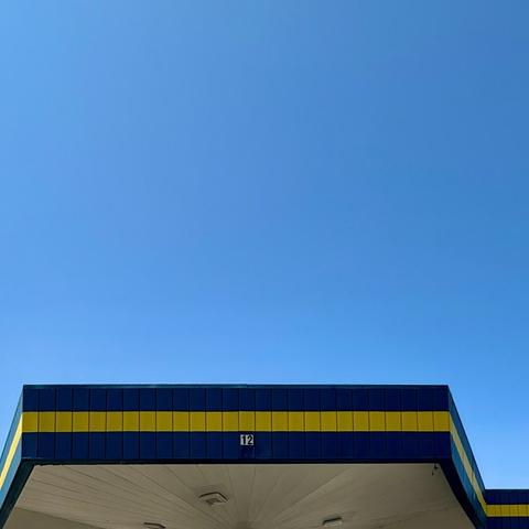 Another angle of the blue and yellow striped gas station canopy showing more of its hexagonal shape. Above is a bright blue sky.