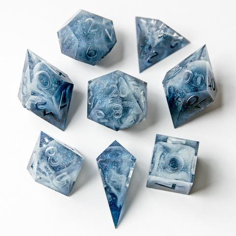 Ein Würfelset in blau/weiß im Inneren. Das Set besteht aus einem D4-Shad, einer D4-Pyramid, D6, D8, D10, D100, D12 und D20. Das Set liegt auf weißem Untergrund mit der höchsten Seite nach oben. Die Würfel sind im Bild um den D20 angeordnet und noch Work in Progress, also nicht geschliffen, poliert oder bemalt.