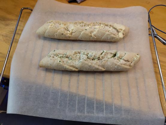 Ein Kräuter- und ein Knoblauchbaguette liegen auf einem Backrost und warten darauf, dass der Backofen heiß wird