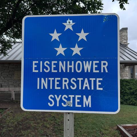 Blue sign with a circle of five white stars at the top, representing the rank of five star General, and the phrase “Eisenhower interstate system”