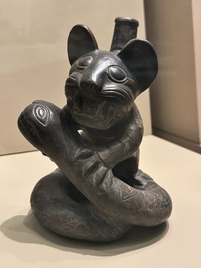 photo of Moche feline with snake blackware effigy vessel #2 at AMNH label at museum: “Ceramic bottle molded and incised to depict a feline grasping a snake. Moche style, Peru. 41.2/8017 Gift of Conny and Fred Landmann”