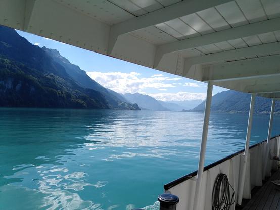 Blick von einem Boot auf blaues Wasser umrundet von Bergen. Blauer Himmel mit ein paar Wolken.