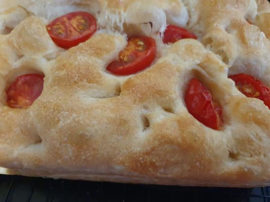 Close up of bubbly, golden brown foccacia with half cherry tomatoes pushed in and baked.