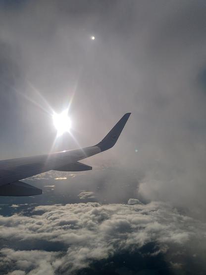 Flügel eines Flugzeuges über Wolken und die Sonne.