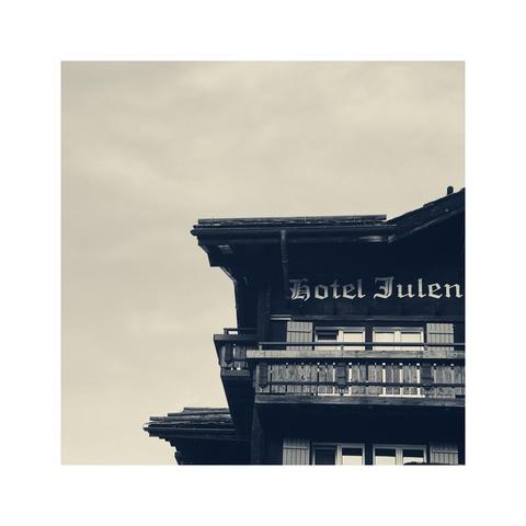 detail of the top floor and some parts of the gabled roof of an old wooden hotel. the name of the hotel "hotel julen" is printed on the almost black facade in white historic letters