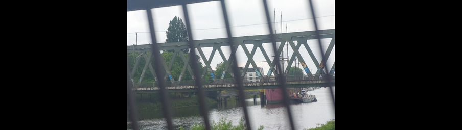 Blick durch das Geländer der Stephanibrücke auf die Eisenbahnbrücke über die Weser. Dahinter liegen ein paar alte Segler als schwimmendes Hotel im Päckchen.