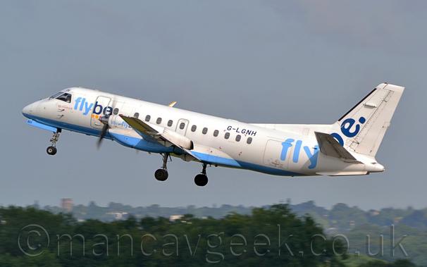 Side view of a white, twin propellor-engined airliner flying from right to left with it's undercarriage lowered, flaps extended from the rear of the wings, and it's nose raised sharply, suggesting it has just taken off.
The plane is mostly white, with a light blue belly, and "FlyBe" titles in light and dark blue on the forward fuselage, repeated in a larger form on the rear fuselage and tail.
There are small, additional red "LoganAir" titles below the cockpit windows.
The registration" G-LGNH" is on the upper rear fuselage in black.
Trees fill the bottom of the frame, slowly vanishing into haze in the distance, with flat grey sky filling the rest.