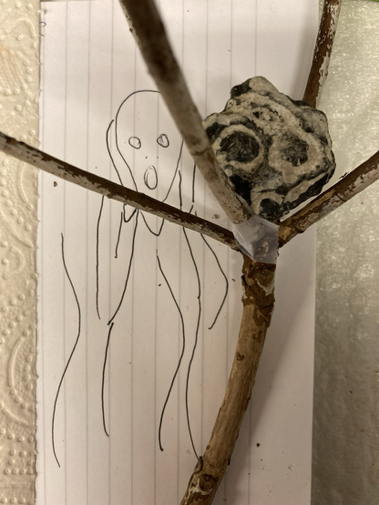 Wooden branch holding a stone that has the expression of Edvard Munch artwork “the scream”. In the background a sketch of that work to isolate the main lines